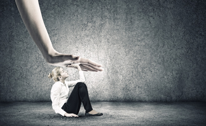 Người ngồi trên sàn, né tránh bàn tay lớn từ trên xuống, trong không gian tối giản màu xám.