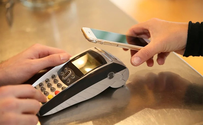 Người dùng đang thực hiện thanh toán không tiếp xúc qua điện thoại di động tại một máy POS trên bàn.