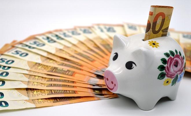 Heo đất trắng với hoa trang trí, bên cạnh là nhiều tờ tiền giấy mệnh giá 50 euro xếp thành hình quạt.