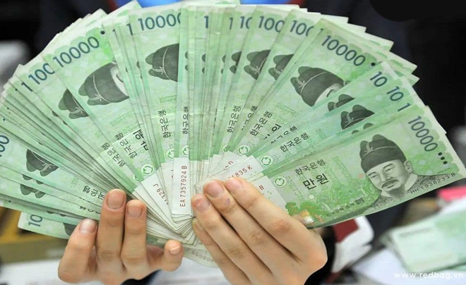 Một người đang cầm một xấp tiền giấy Hàn Quốc mệnh giá 10.000 won, xòe ra thành hình quạt.