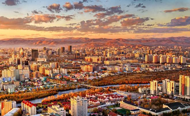 Quang cảnh thành phố với nhiều tòa nhà cao tầng, đường phố và dòng sông, ánh sáng hoàng hôn chiếu rọi.