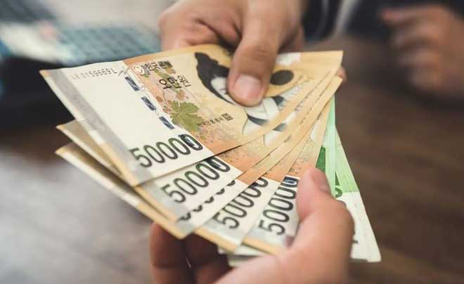 Hai tay trao đổi một xấp tiền giấy Hàn Quốc mệnh giá 50.000 won trên nền bàn gỗ.