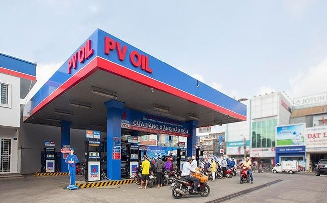Trạm xăng với nhiều xe máy đang đổ xăng, có biển hiệu PV OIL trên mái che, nền trời xanh.
