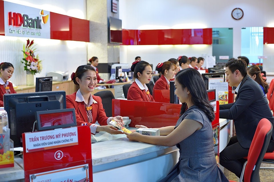 Khách hàng giao dịch tại quầy trong một ngân hàng với nhân viên mặc đồng phục đỏ và đen.