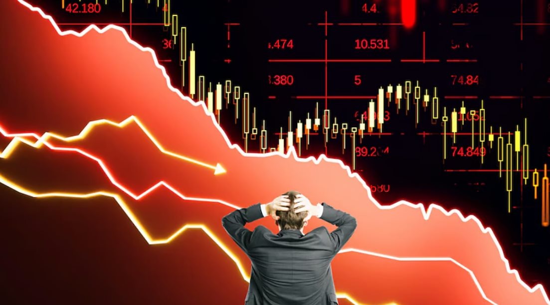 Người đàn ông cầm đầu trước biểu đồ tài chính có xu hướng giảm mạnh, nền màu đỏ biểu thị sự sụt giảm.