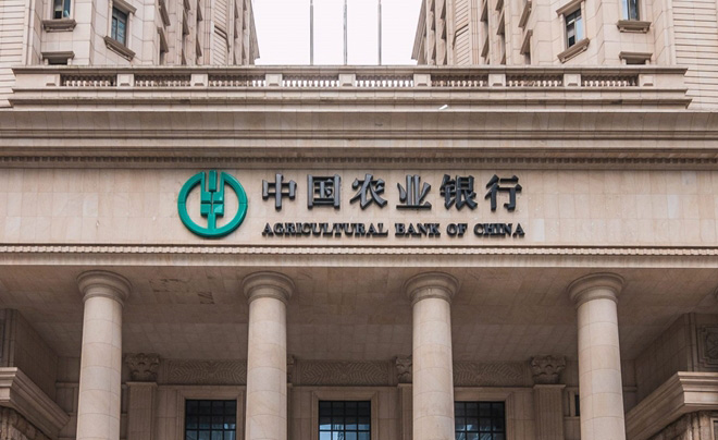 Mặt tiền tòa nhà ngân hàng với tên và logo "Agricultural Bank of China" trên nền cột trụ kiến trúc cổ điển.