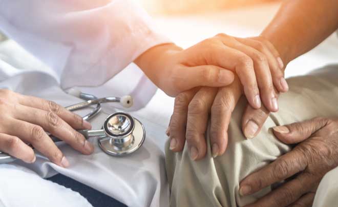 Bàn tay một người được đặt lên tay người khác, cạnh đó là ống nghe y tế, thể hiện sự an ủi và chăm sóc.