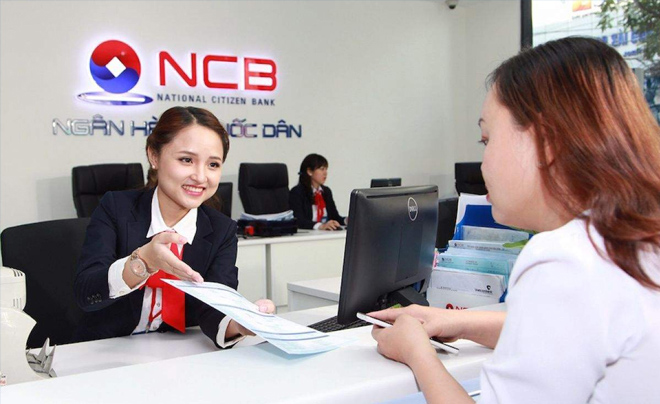 Nhân viên ngân hàng đang trao đổi tài liệu với khách hàng tại quầy giao dịch, bên trong chi nhánh ngân hàng.