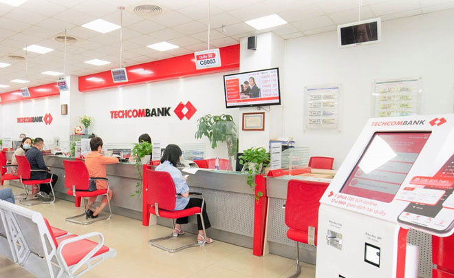 Khách hàng đang giao dịch tại quầy trong một chi nhánh ngân hàng với thiết kế nội thất hiện đại và tông màu đỏ.