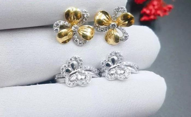 Bông tai hoa đính đá, hai đôi: một đôi vàng và một đôi bạc, được đặt trên nền găng tay trắng.