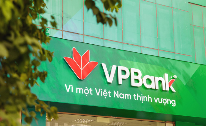 Mặt tiền ngân hàng với logo và khẩu hiệu trên biển hiệu xanh, cây xanh phía trước.