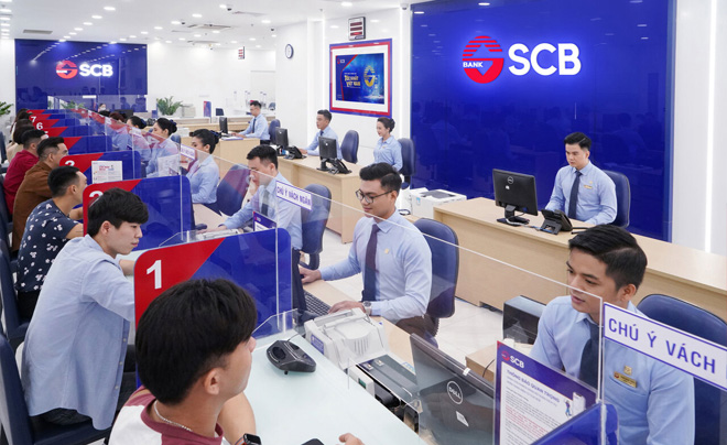 Ngân hàng với nhiều khách hàng ngồi tại quầy giao dịch và nhân viên làm việc tại máy tính trong không gian hiện đại.