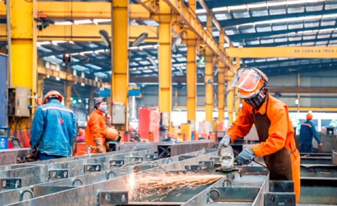 Công nhân trong nhà máy, người sử dụng máy mài cầm tay, tia lửa bay ra, mặc đồ bảo hộ màu cam.