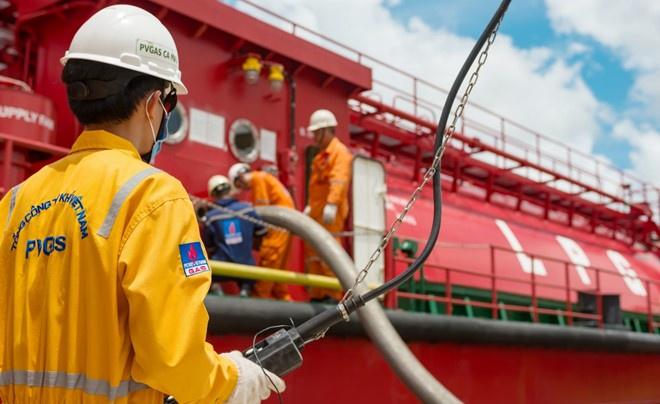 C&ocirc;ng nh&acirc;n mặc đồ bảo hộ m&agrave;u cam đang l&agrave;m việc tr&ecirc;n t&agrave;u chở h&agrave;ng m&agrave;u đỏ, c&oacute; d&acirc;y c&aacute;p v&agrave; ống dẫn.