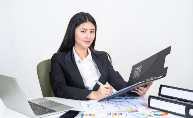 Người phụ nữ mặc vest đen ngồi tại bàn làm việc với laptop và tài liệu.
