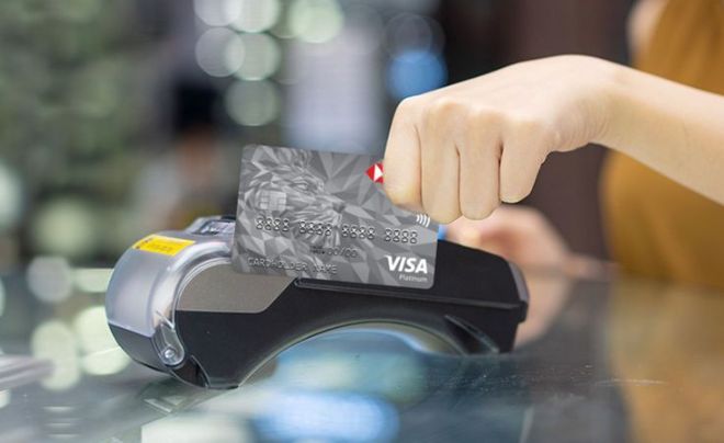 Một tay đang quẹt thẻ ngân hàng qua máy POS trên bề mặt kính trong môi trường mờ ảo.
