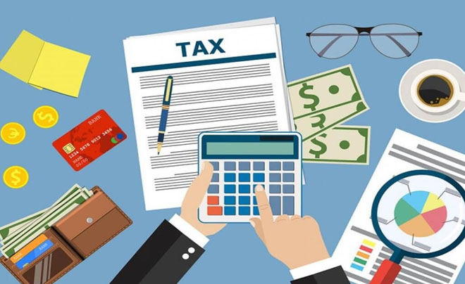 Bàn làm việc với tài liệu thuế, máy tính, biểu đồ, tiền mặt, cà phê, ví tiền, kính và thẻ ngân hàng.