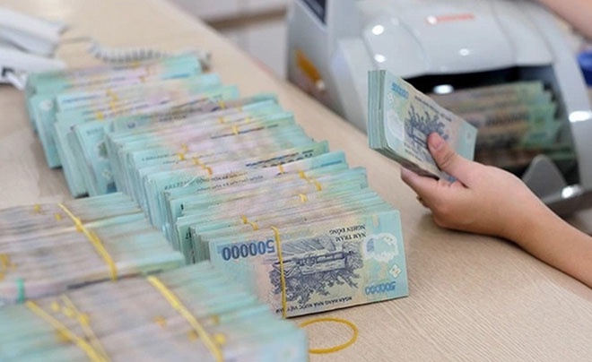 Một bàn tay đang đếm các tập tiền Việt Nam mệnh giá lớn đặt trên bàn.