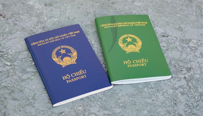 Hai cuốn hộ chiếu Việt Nam, một màu xanh dương và một màu xanh lá, đặt trên nền đá xám.
