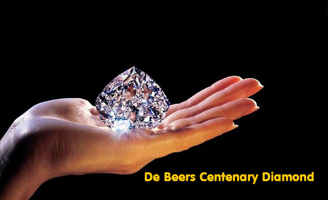 Bàn tay nâng viên kim cương lớn, sáng bóng trên nền đen, với dòng chữ "De Beers Centenary Diamond" màu vàng phía dưới.
