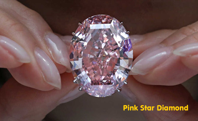 Đôi tay cầm viên kim cương màu hồng lớn, hình bầu dục, lấp lánh, có dòng chữ “Pink Star Diamond”.