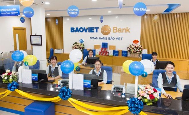 Nhân viên ngân hàng ngồi tại quầy giao dịch, trang trí bằng bóng bay và hoa, trong không gian hiện đại.