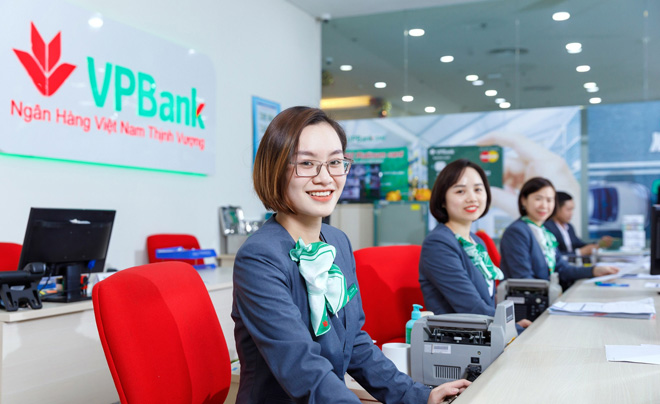 Nhân viên ngân hàng ngồi tại quầy giao dịch trong văn phòng hiện đại, mặc đồng phục chuyên nghiệp và tươi cười.