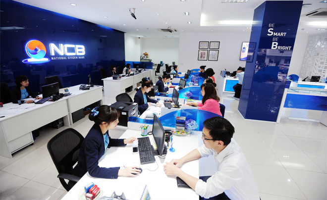 Ngân hàng với nhân viên đang làm việc tại bàn giao dịch, không gian hiện đại, logo NCB trên tường.