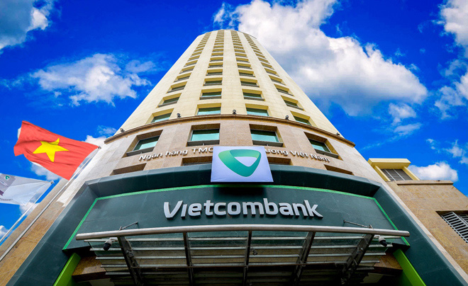 Tòa nhà cao tầng của Vietcombank với bầu trời xanh và lá cờ Việt Nam bay phía trước.