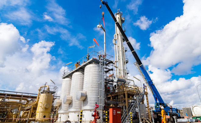 Nh&agrave; m&aacute;y c&ocirc;ng nghiệp với c&aacute;c bồn chứa lớn v&agrave; cần cẩu, trời xanh nhiều m&acirc;y.