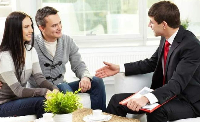 Một cặp đôi trò chuyện với người tư vấn trong văn phòng, bàn có sách, tách trà và cây xanh.
