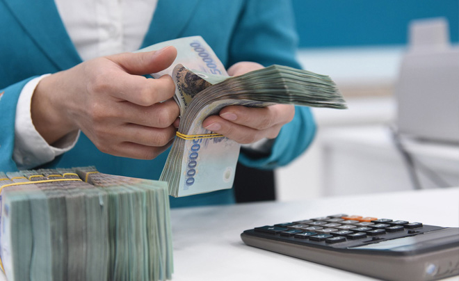 Người đếm tiền giấy bên cạnh một máy tính cầm tay trên bàn.