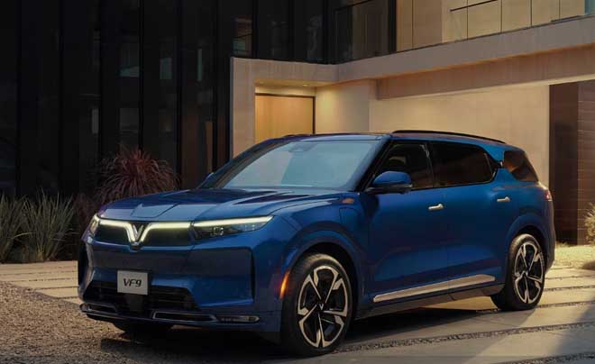Xe SUV màu xanh đậu trước một tòa nhà hiện đại vào buổi tối, có biển số ghi "VF9".
