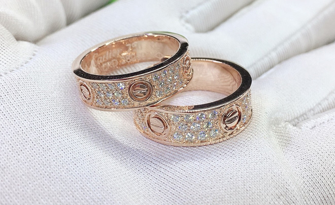 Hai chiếc nhẫn vàng hồng đính đá lấp lánh, đặt trên nền vải trắng, thiết kế tinh xảo và sang trọng.