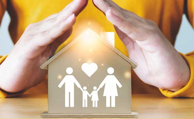 Hai bàn tay che chở mô hình ngôi nhà với biểu tượng gia đình và trái tim, tượng trưng cho sự bảo vệ và tình yêu.