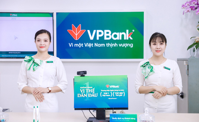 Hai nhân viên đứng tại quầy dịch vụ khách hàng của ngân hàng VPBank với màn hình quảng cáo phía sau.