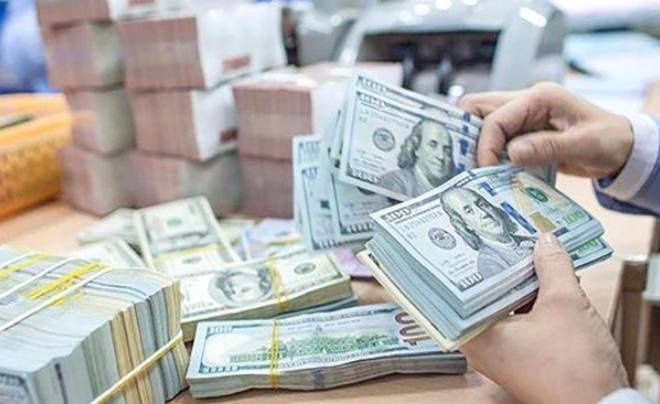 Hai tay đang đếm các cọc tiền đô la Mỹ, xung quanh là nhiều cọc tiền khác nhau trên bàn.