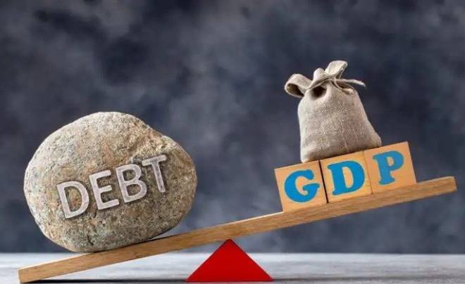 Hình ảnh một tảng đá ghi chữ "DEBT" và túi tiền trên bập bênh, biểu thị sự cân bằng giữa nợ và GDP.