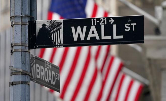 Biển chỉ đường Wall St và Broad St với cờ Mỹ mờ phía sau.