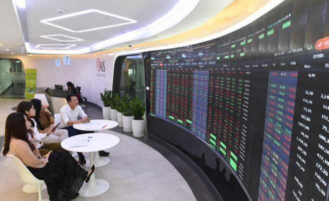 Một nhóm người ngồi trước màn hình lớn hiển thị thông tin thị trường chứng khoán trong không gian hiện đại.