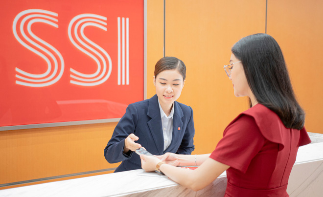 Hai người đang trao đổi tại quầy lễ tân trong văn phòng có logo SSI trên tường.