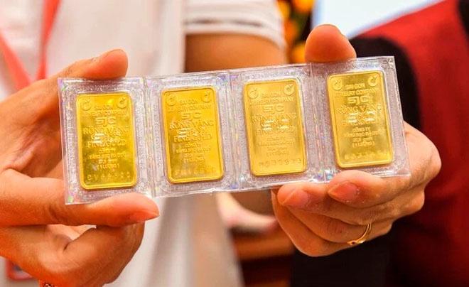 Hai tay đang cầm bốn thỏi vàng nhỏ, được đặt trong khung nhựa bảo vệ trong suốt.