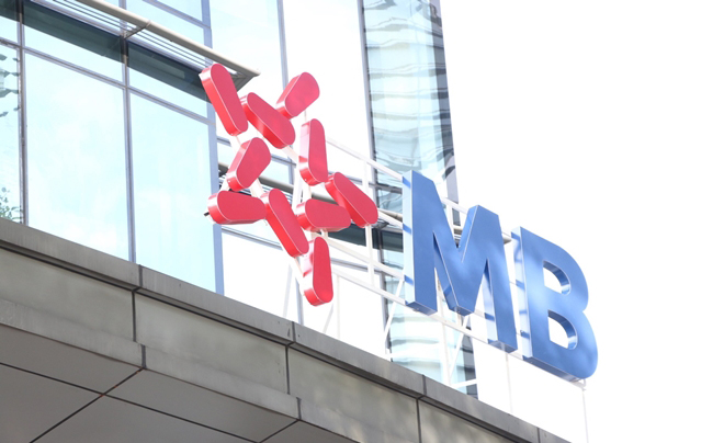 Logo và chữ trên tòa nhà kính, có phần chữ "MB" màu xanh và hình ngôi sao đỏ.