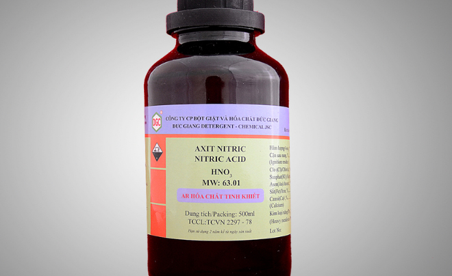 Chai thủy tinh chứa axit nitric, nhãn ghi thông tin hóa chất và cảnh báo an toàn.