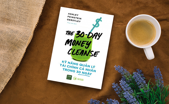 Sách "The 30-Day Money Cleanse" trên bàn nâu, bên cạnh là tách cà phê và bó hoa oải hương.