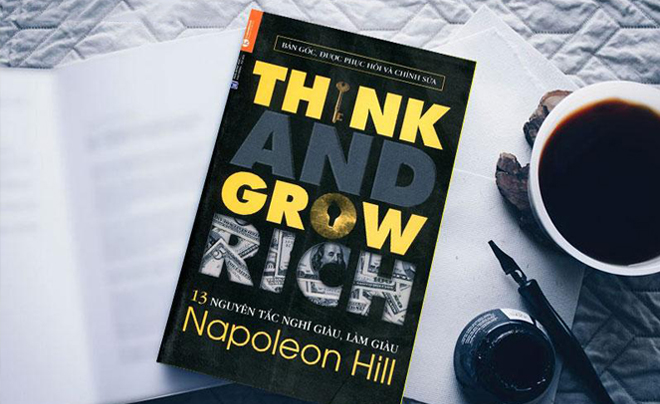 Cuốn sách "Think and Grow Rich" nằm trên bàn cạnh tách cà phê và bút viết.