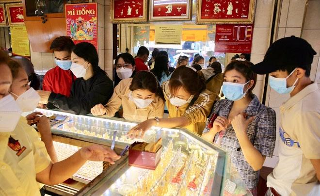 Khách hàng đeo khẩu trang đang chọn lựa trang sức tại một cửa hàng vàng, với nhân viên hỗ trợ phía sau quầy kính.
