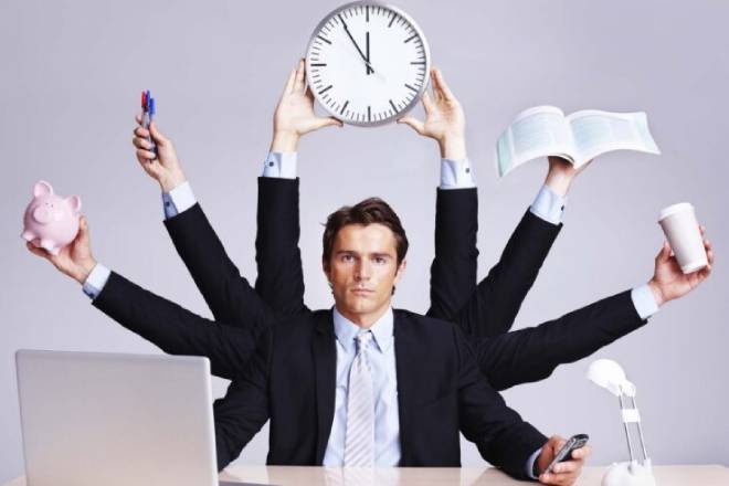 Người đàn ông trong trang phục công sở với nhiều cánh tay cầm đồng hồ, sách, cốc, heo đất và bút.
